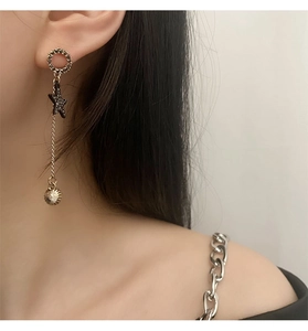 Detail of long gold earrings featuring a black star and textured spiral ball pendant
