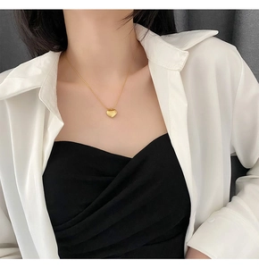 Detail of a polished gold heart pendant necklace on a model wearing a white shirt