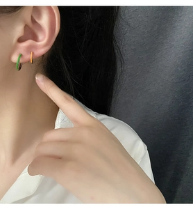 Primer plano de pendientes de aro verde brillante y naranja con una camisa blanca lisa