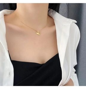 Close-up of a gold ginkgo leaf pendant necklace worn by a model over a white shirt