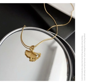 Macro shot of gold ginkgo leaf pendant necklace reflecting on a vanity mirror