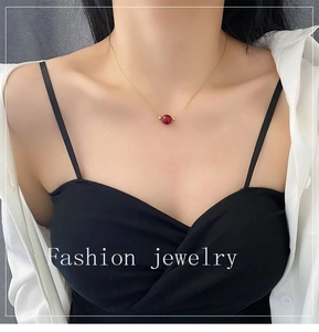 Close-up of a delicate gold titanium necklace with a single red bean bead on a female model