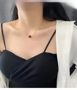 Close-up of minimalist gold titanium necklace with a single red agate bead on a model