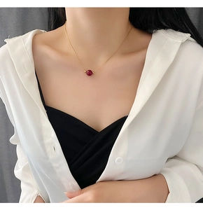Minimalist gold necklace with red bead pendant worn by a model to show length and drop