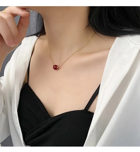 Close-up of a delicate gold snake chain necklace with a single red bean bead pendant