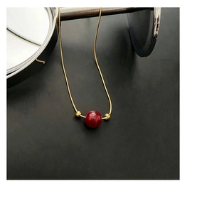 Macro shot of a red bead on a gold snake chain necklace over a black matte background