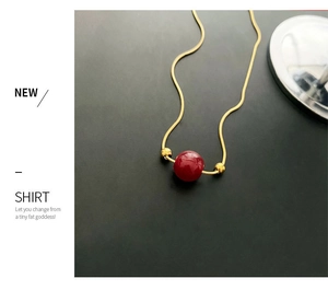 Detail of a minimalist gold snake chain necklace with a round red bead pendant