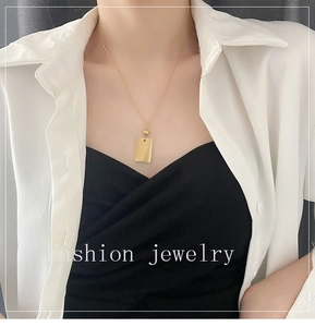 Primo piano di una collana con ciondolo rettangolare dorato minimalista su camicia bianca