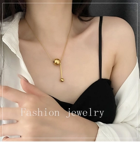 Gros plan d'un collier doré minimaliste avec perles de différentes tailles sur un mannequin