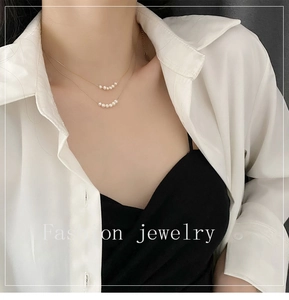 Detail of layered gold titanium necklace with natural pearls on a white shirt
