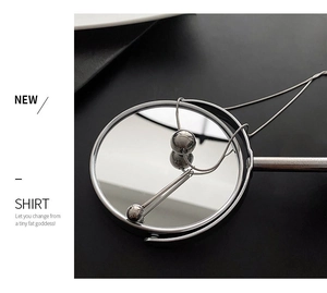 Collier géométrique argenté minimaliste avec pendentifs boule et cylindre sur un miroir