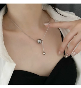Vue détaillée du collier géométrique argenté avec pendentif sphère et barre sur modèle
