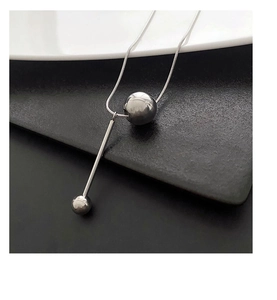 Vue macro d'un collier géométrique argenté avec perles polies sur fond texturé contrasté