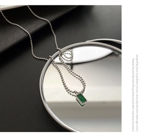 Dettaglio macro di una collana a sfere d'argento con un ciondolo rettangolare verde smeraldo