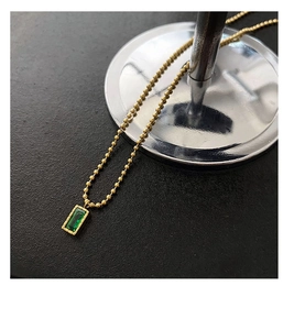 Dettaglio della catena a sfere in oro 18k con un ciondolo rettangolare verde smeraldo
