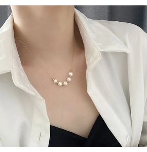 Détail d'un élégant collier doré avec cinq perles blanches porté par un mannequin