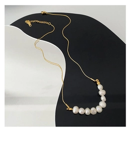 Détail du collier en chaîne dorée avec huit perles blanches et fermoir mousqueton
