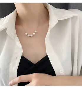 Gros plan de cinq perles blanches sur une chaîne en acier titane portée par un mannequin