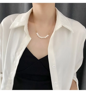 Collier élégant en titane doré avec sept perles blanches porté sur la clavicule d'une femme