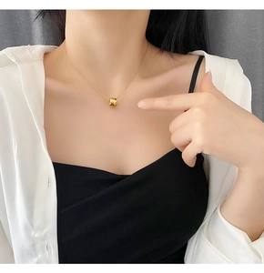 Detail of gold rhombus-cut cylinder pendant necklace worn by a female model