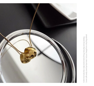 Detail of faceted gold cylinder pendants on fine chain reflected on a round mirror
