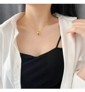 Close-up of a gold faceted cylinder pendant necklace worn by a model on a delicate chain