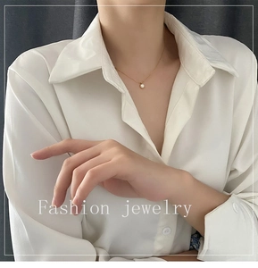 Detail of a minimalist gold necklace with a round white pearl pendant worn on a model