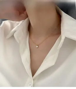 Detail of a minimalist gold tone necklace with a white round pendant on a female model