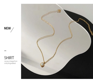 Macro detail of minimalist gold pendant necklace featuring a white opal stone on a mirror