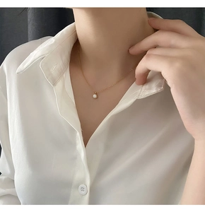 Close-up of minimalist gold titanium necklace with white shell pendant on a model