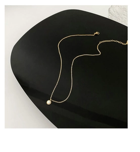 Close-up of minimalist gold necklace with round white shell pendant on dark display