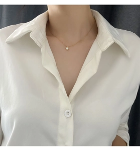 Close-up of a gold chain necklace with a round white shell pendant worn by a model in a white shirt