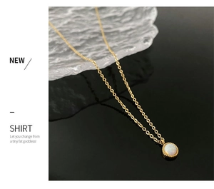 Detail of a gold titanium necklace featuring a white opal pendant on a reflective surface