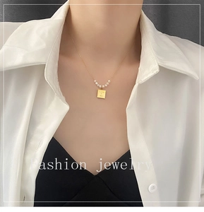 Detailed view of gold pearl necklace with square pendant engraved with Love Me text
