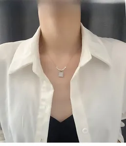 Close-up of a silver stamp pendant necklace with pearls on a model wearing white