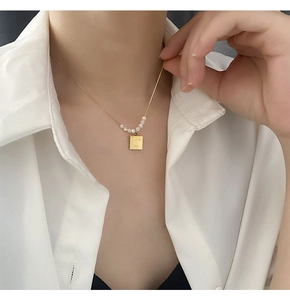Detailed view of gold rectangle stamp pendant with Love Me engraving and pearls