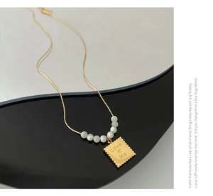 Detail of gold necklace featuring a Love Me engraved rectangular pendant and shell beads