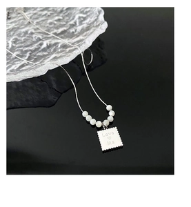 Detail view of a shell pendant necklace with Love Me engraving and white pearl accents