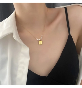 Detail of gold necklace featuring 5 pearls and a square charm engraved with Love Me text