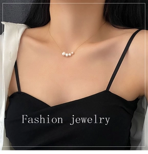 Detailed view of four natural pearls on a gold titanium steel necklace worn by a model