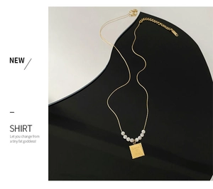 Close-up of gold square pendant with Love Me engraving and white beads on thin chain