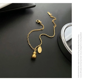 Macro detail of 18k gold plated titanium gourd charm and lucky coin pendant bracelet