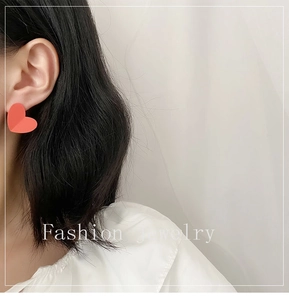Close-up of a model wearing a large coral red heart earring with a textured matte finish