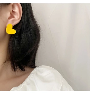 Close-up of bright yellow heart stud earrings with matte finish on a female model