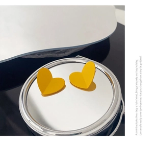 Macro shot of matte yellow heart-shaped stud earrings on a metallic display stand