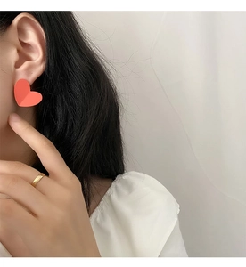 Detail shot of a matte pink heart earring and a simple gold ring worn by a model