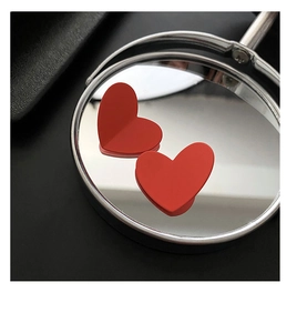 Detailed close-up of red matte heart earrings reflecting on a round metallic mirror surface