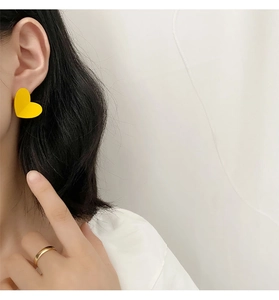 Close-up of a model wearing matte yellow heart earrings and a simple gold ring