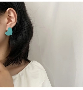 Close-up of a model wearing matte turquoise heart-shaped stud earrings with a white top