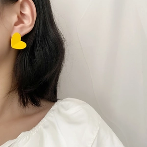 Minimalist matte yellow heart stud earrings worn by a model in a bright setting